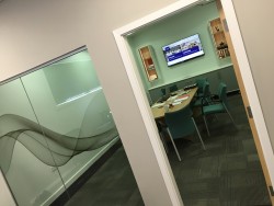 External view of meeting room showing glazed wall section with swirl manifestation, bespoke meeting room storage units and cable connected wall mounted TV for presentations