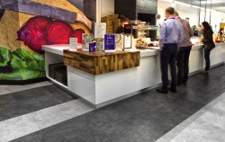 Bespoke servery counters with Corian worktops, gloss laminate front panels, walnut capping corner sections with large beetroot graphic and stone effect vinyl flooring