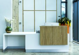 Concirege Desk and wall panelling, desk finsihed in White Corian with brushed effect stainless steel laminate kikc plinths and woodgrain feature boxes, wall paneeling behind to match finishes and hide access door